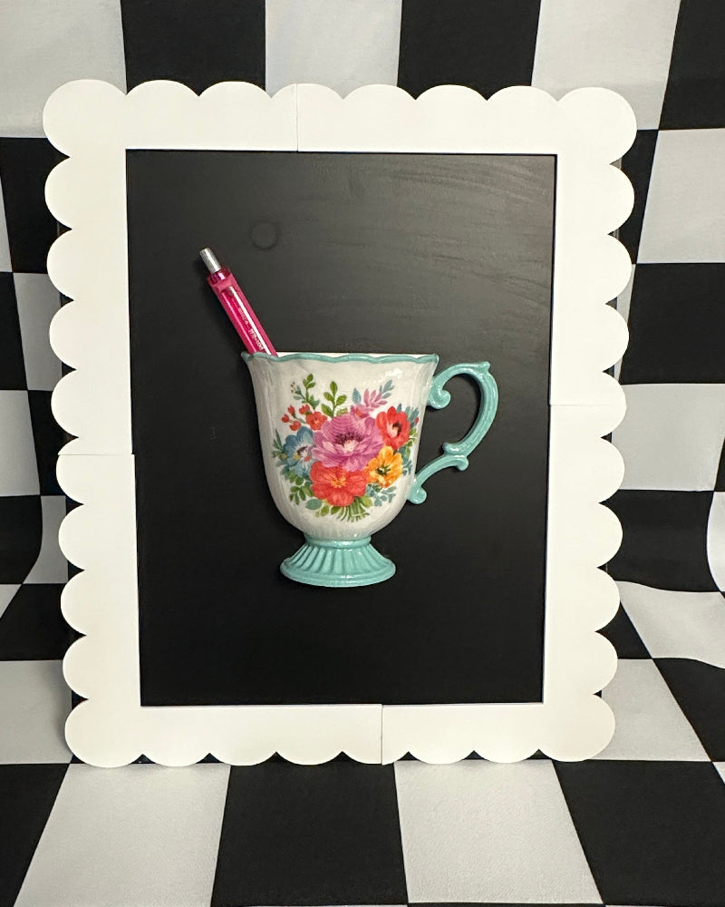 Floral teacup with a pen on a blackboard against a black and white checkered background