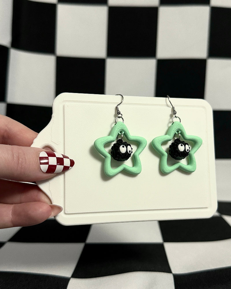 Star-shaped earrings on a card held by a hand against a checkered background