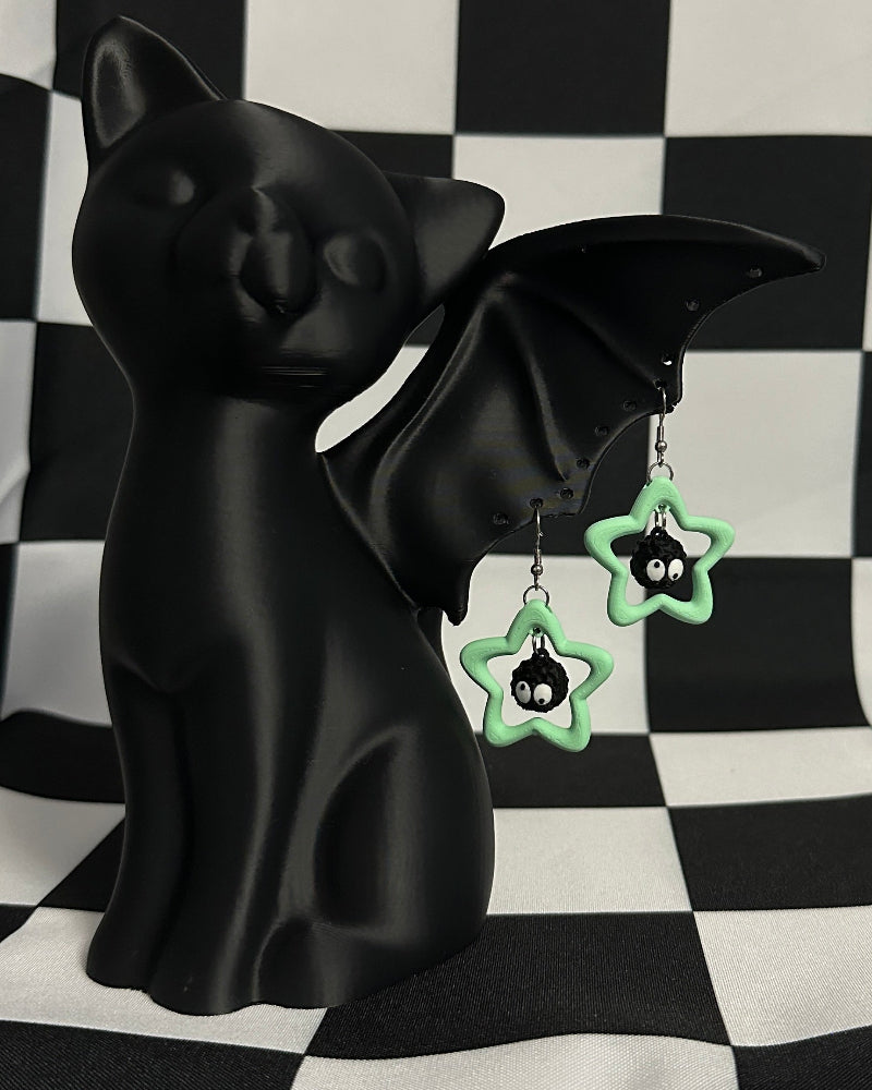 Black bat-shaped figurine with green earrings on a black and white checkered background
