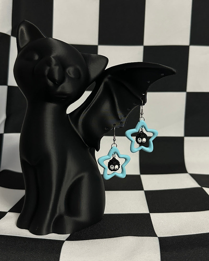 Black cat figurine with bat wings and star-shaped earrings on a black and white checkered background