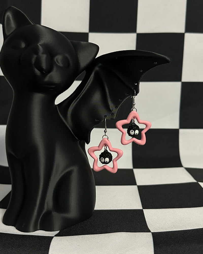 Black cat figurine with pink star-shaped earrings on a black and white checkered background
