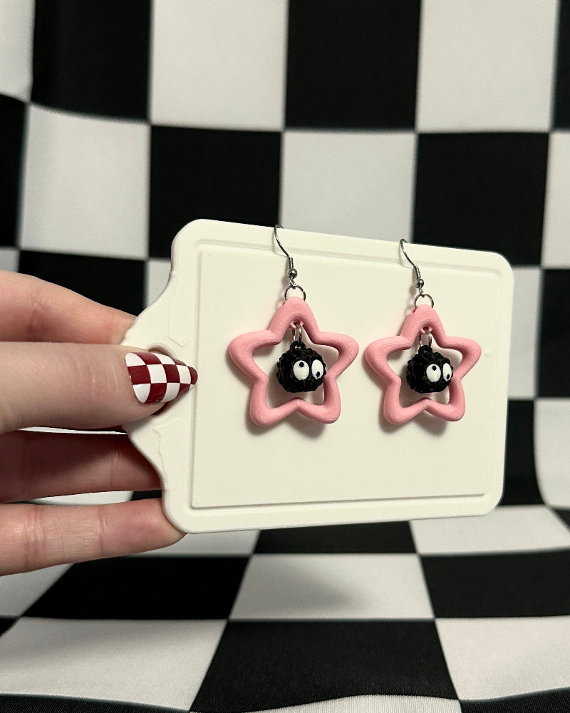Star-shaped earrings with black centers held against a checkered background