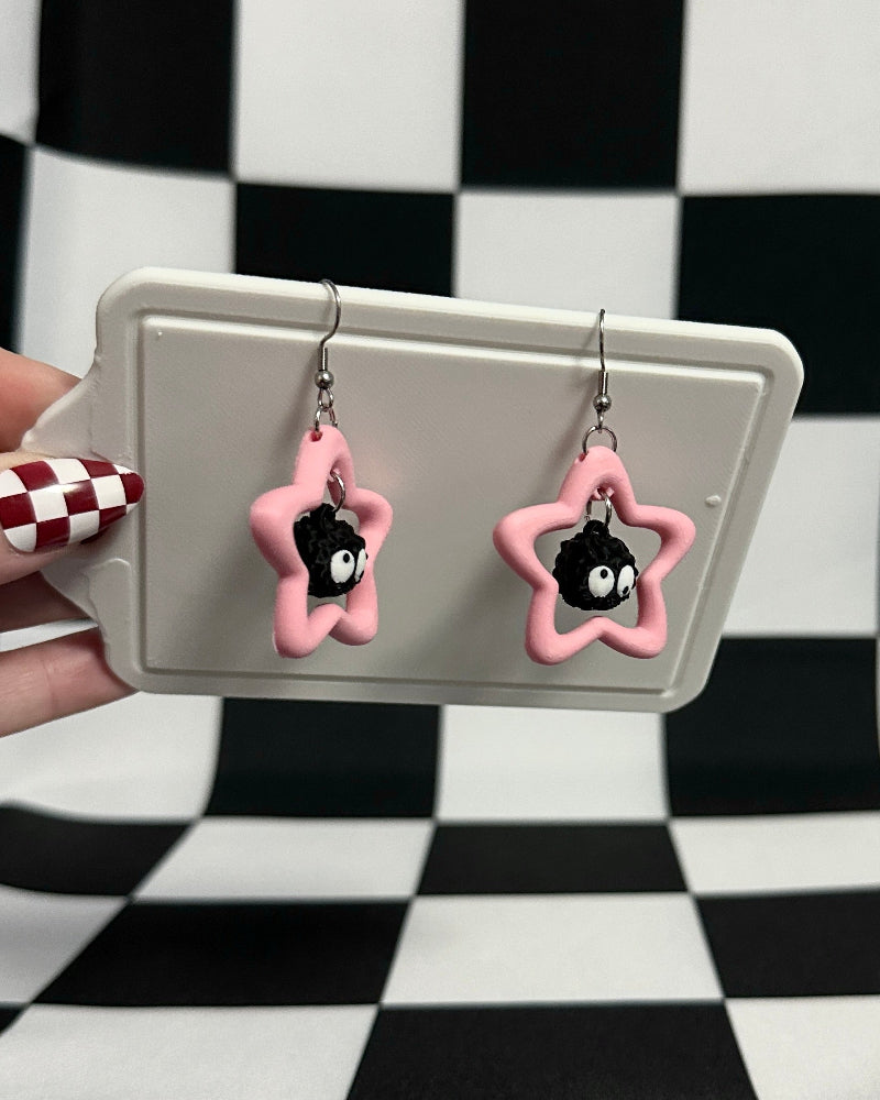 Pink star-shaped earrings on a gray card against a black and white checkered background