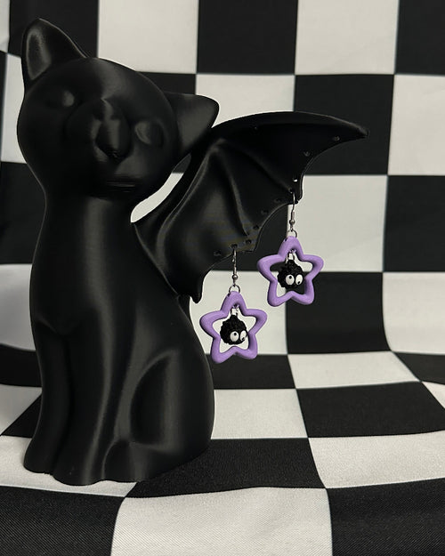 Black bat figurine with purple flower-shaped earrings on a black and white checkered background