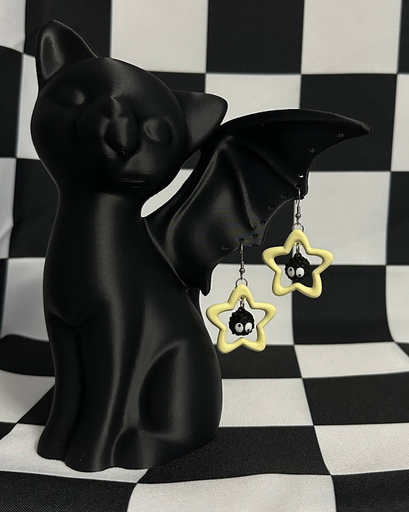 Black cat figurine with star-shaped earrings on a black and white checkered background