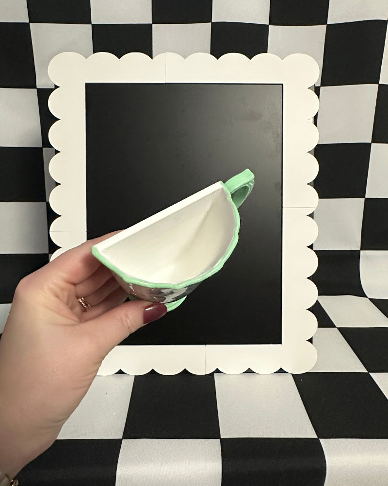 Hand holding a ceramic teapot against a black and white checkered background
