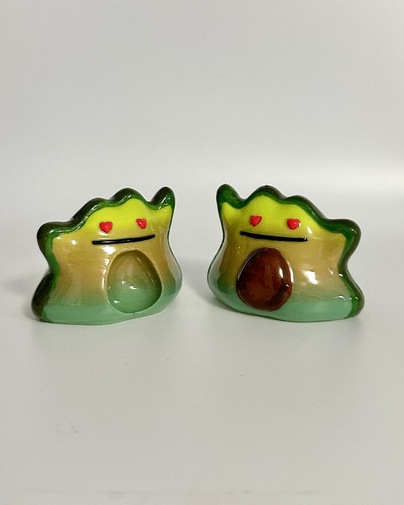 Two small figurines resembling avocados with faces on a white surface.