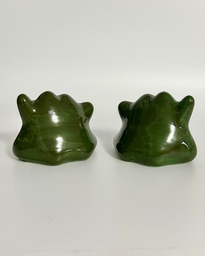 Two avocado-shaped objects on a white surface with a clear glass container in the background.