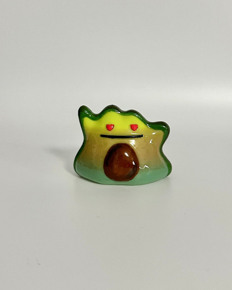 Small figurine of a creature with a green body, brown head, and red eyes on a white background.