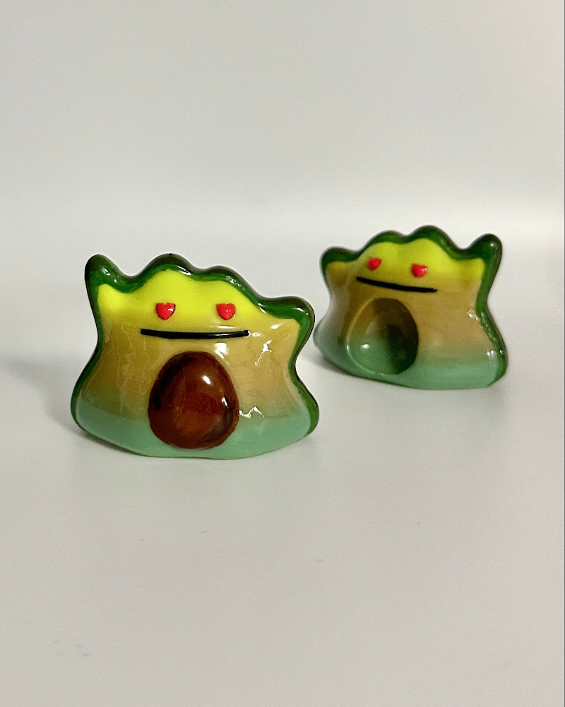 Two small figurines of avocados with facial expressions on a white background