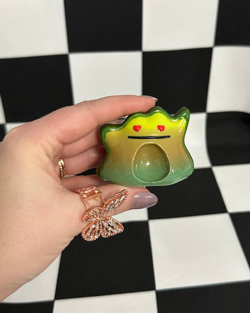 Hand holding a small green creature toy on a black and white checkered background