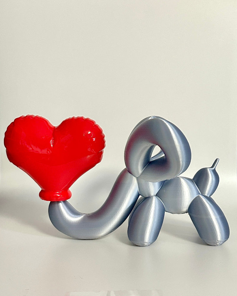 Decorative balloon animal and heart-shaped object on a shelf with a checkered curtain in the background.