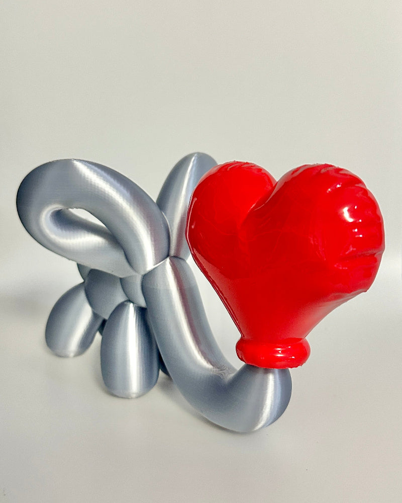 Balloon animal sculpture with a red heart and silver body on a white surface.