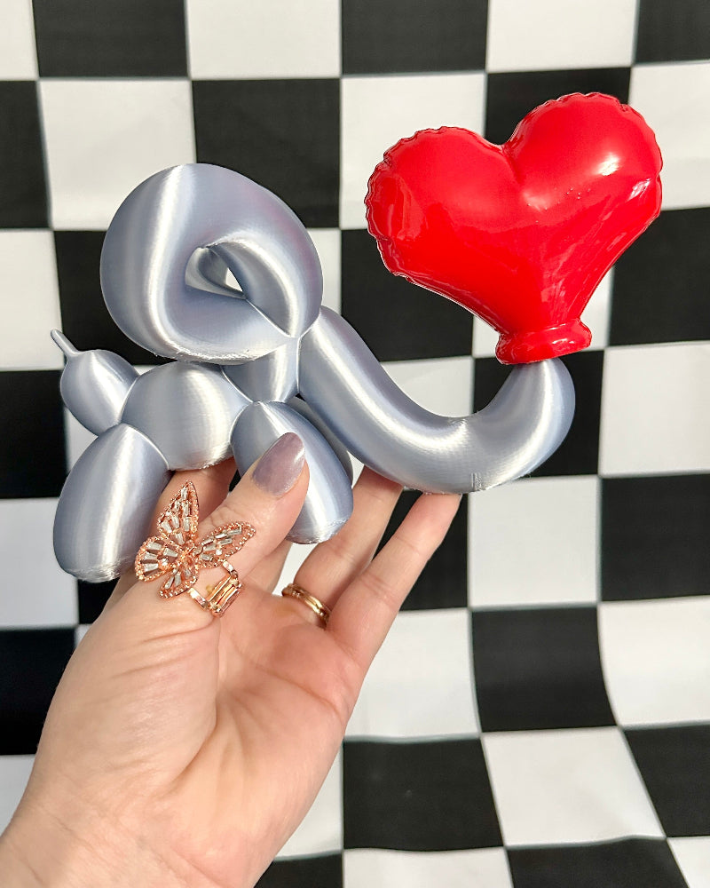 Metallic 'I' and heart-shaped object held by a hand against a checkered background