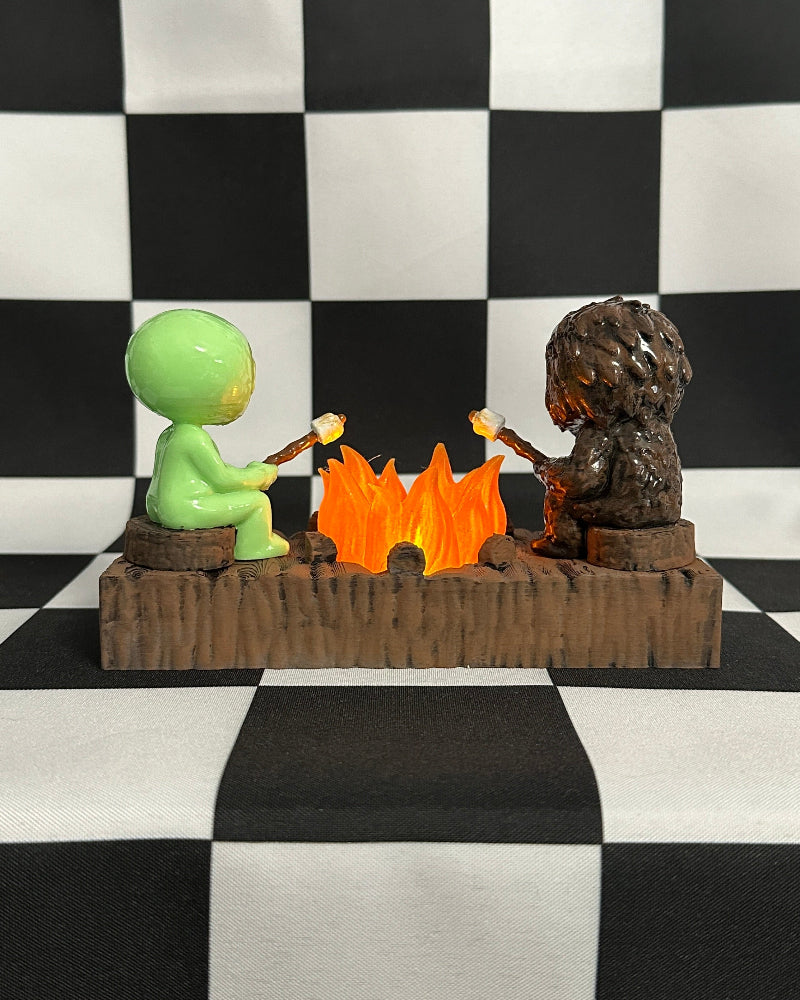 Two small figurines by a campfire on a black and white checkered background