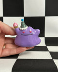 Hand holding a purple cartoon-like figurine with a checkered background