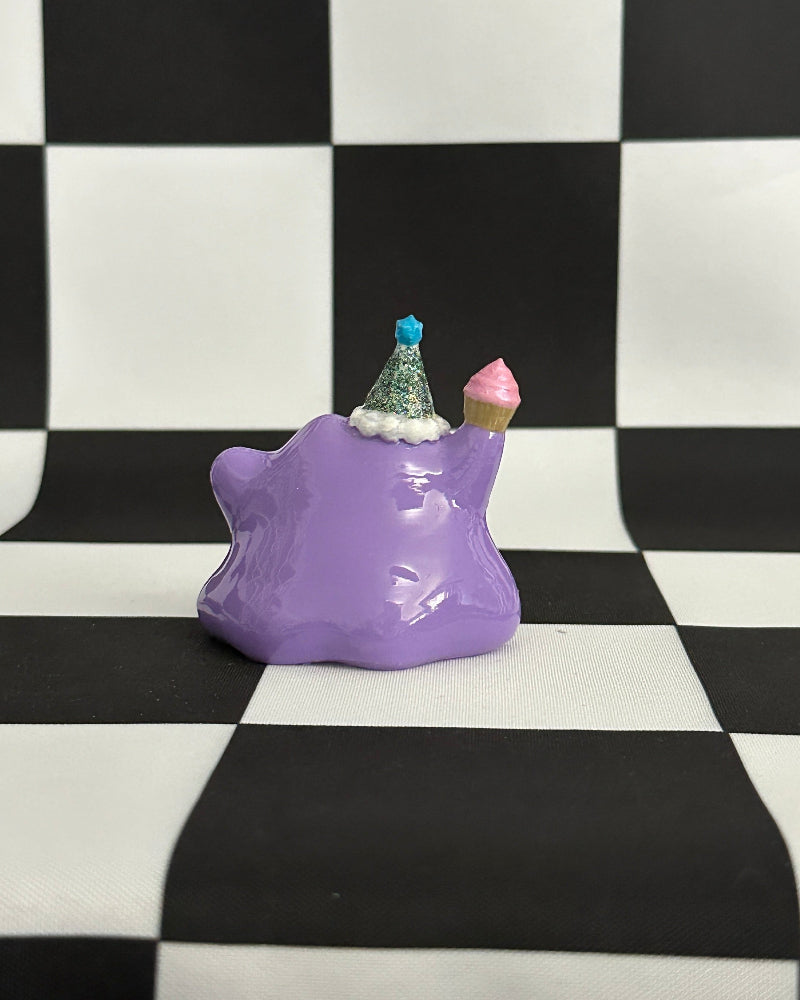Purple cat-shaped object with small decorative items on a black and white checkered background