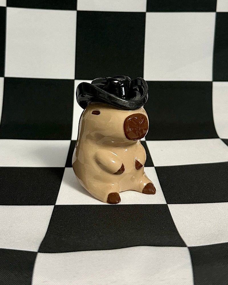 Small figurine of a capybara wearing a graduation cap on a black and white checkered background