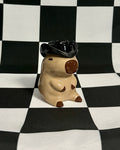 Small figurine of a capybara wearing a graduation cap on a black and white checkered background