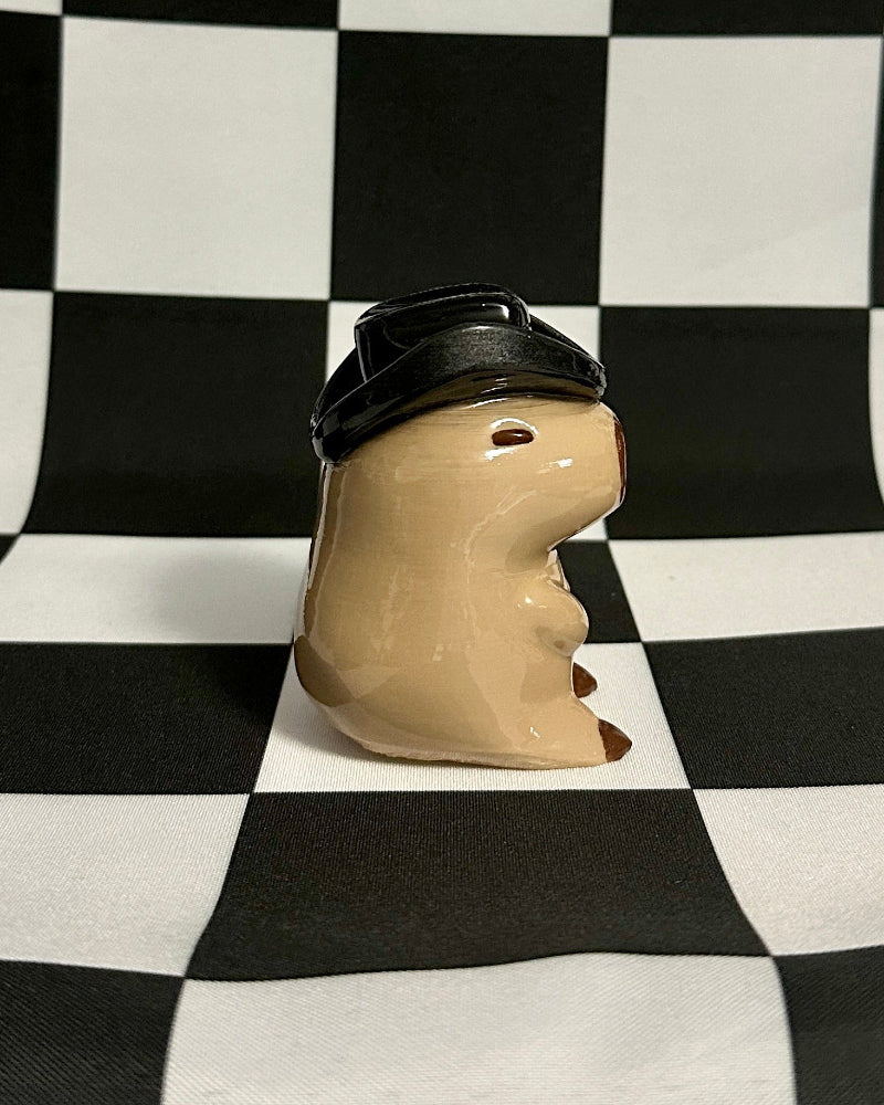 Small animal figurine wearing a black hat on a checkered background