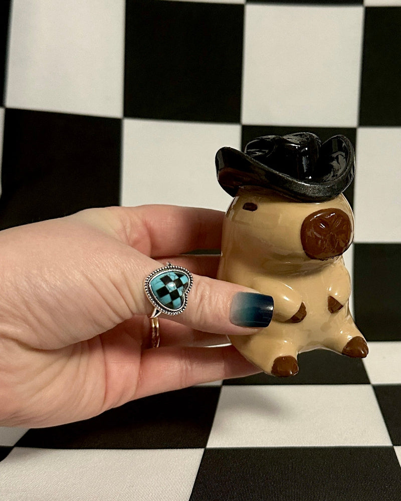 Small figurine held by a hand against a black and white checkered background
