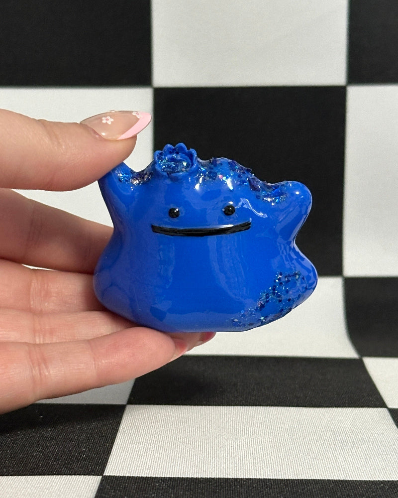 Blue creature-shaped object held by a hand on a black and white checkered background