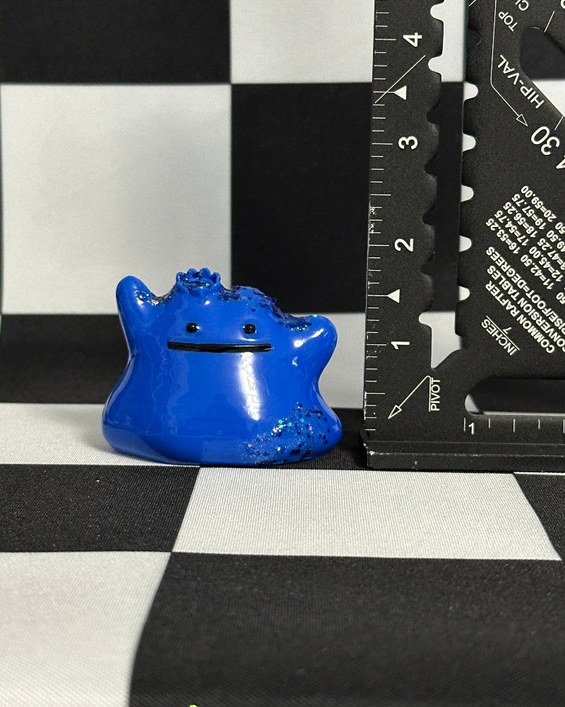 Blue creature figurine next to a ruler on a checkered background