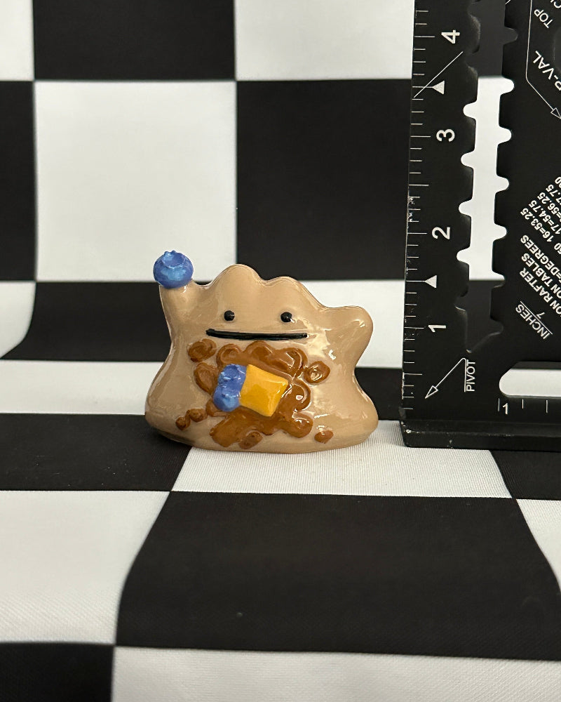 Small figurine on a black and white checkered surface with a ruler for scale.