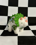 Small white dinosaur figurine with green spikes on a black and white checkered background