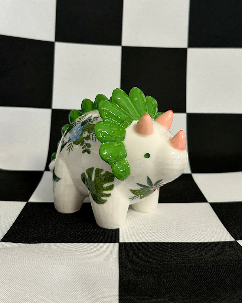 Small white dinosaur figurine with green spikes on a black and white checkered background