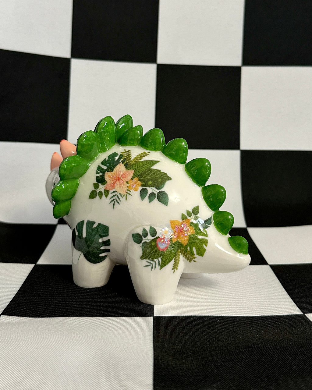 Decorative dinosaur figurine with floral patterns on a black and white checkered background