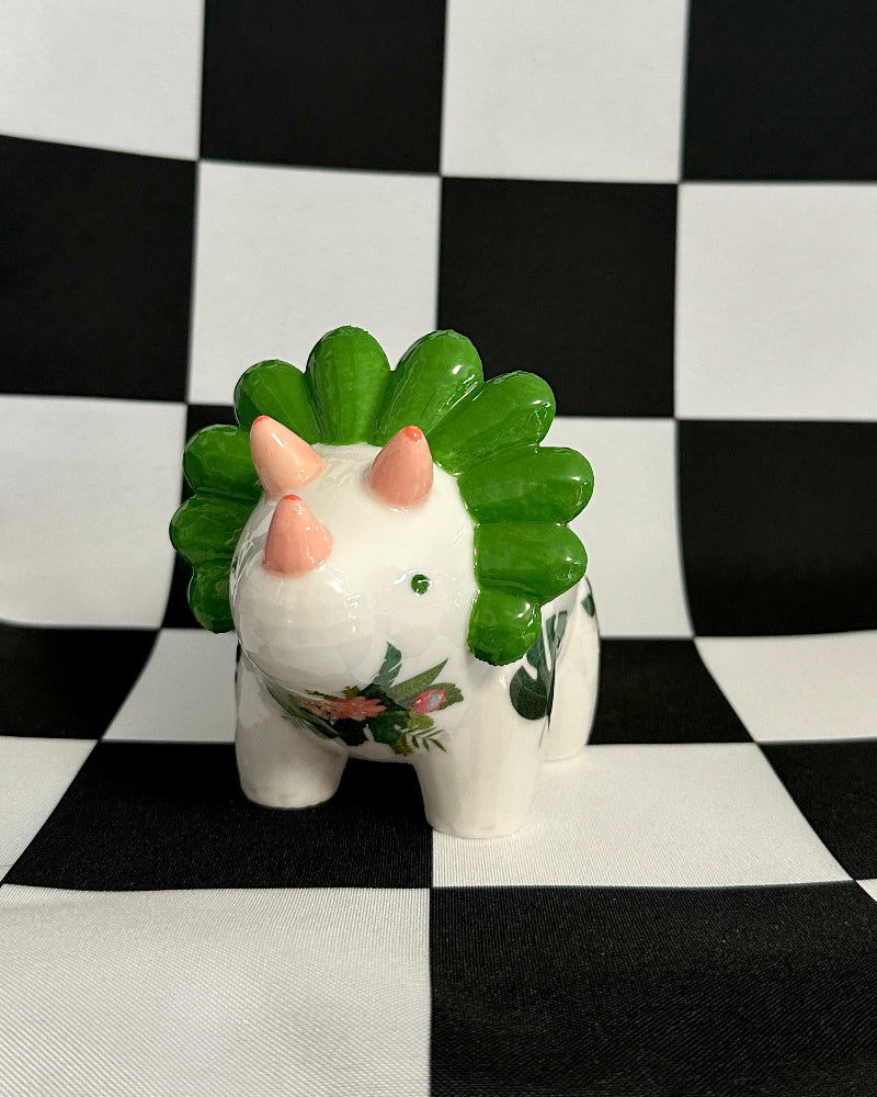 Small white ceramic animal figurine with green spiky hair on a black and white checkered background