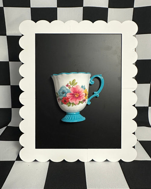 Green teacup with floral pattern on a black background, framed by a white scalloped border against a black and white checkered wall.