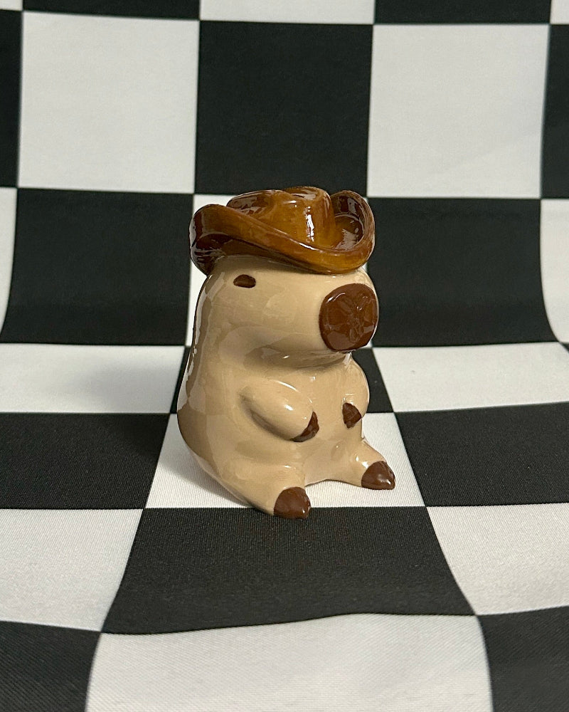 Small figurine of a creature with a brown hat on a checkered black and white background