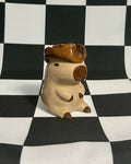 Small figurine of a creature with a brown hat on a checkered black and white background