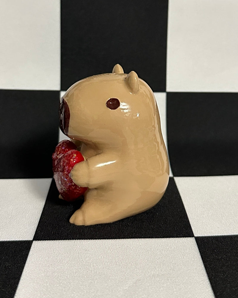 Small beige figurine of a creature holding a red object on a black and white checkered background