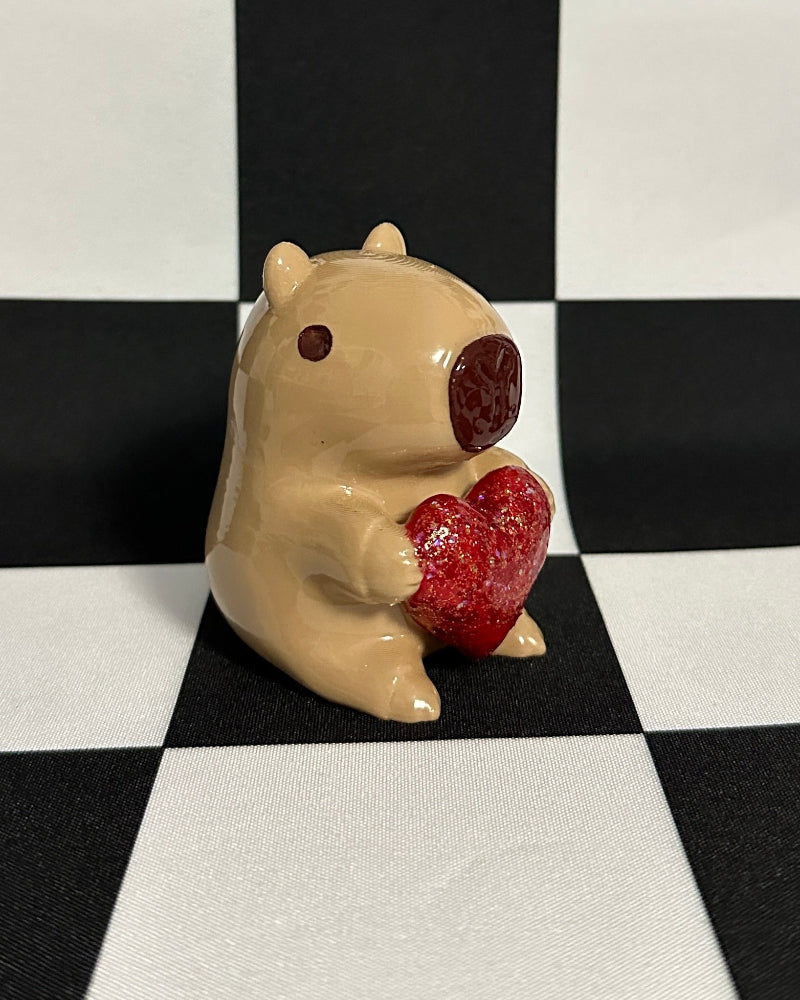 Small figurine of a capybara holding a red heart on a black and white checkered background
