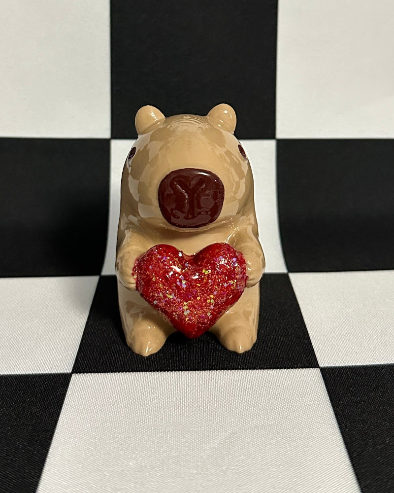 Small capybara figurine with a red heart on a black and white checkered background