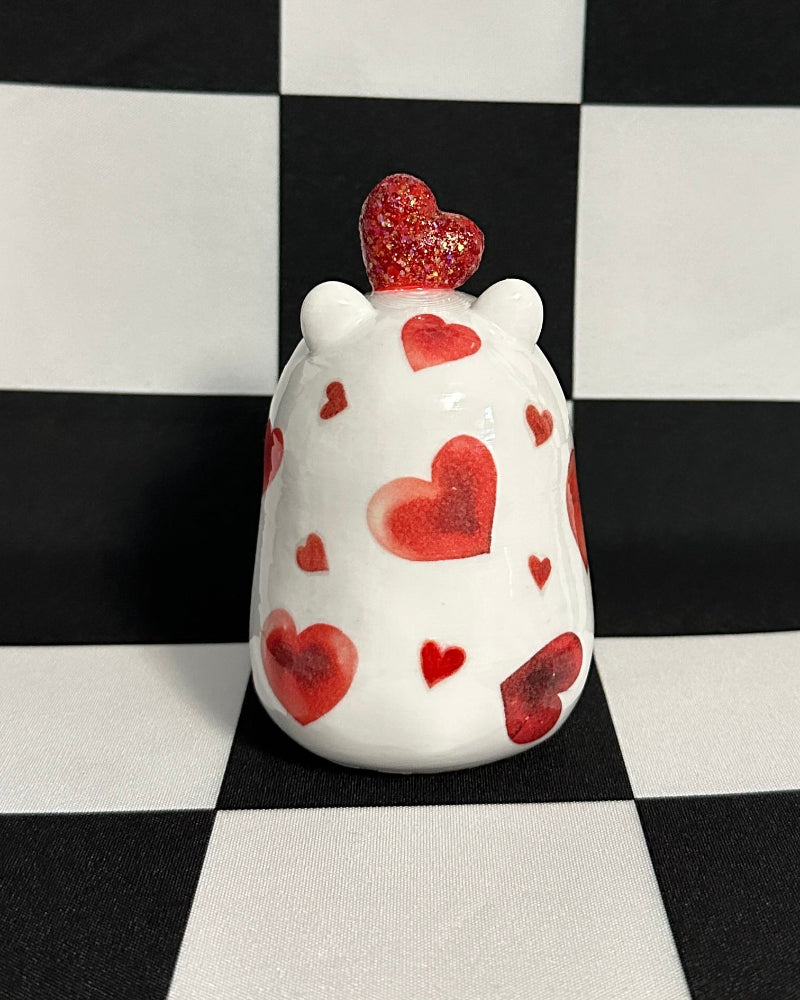 White capybara figurine with red heart patterns on a black and white checkered background