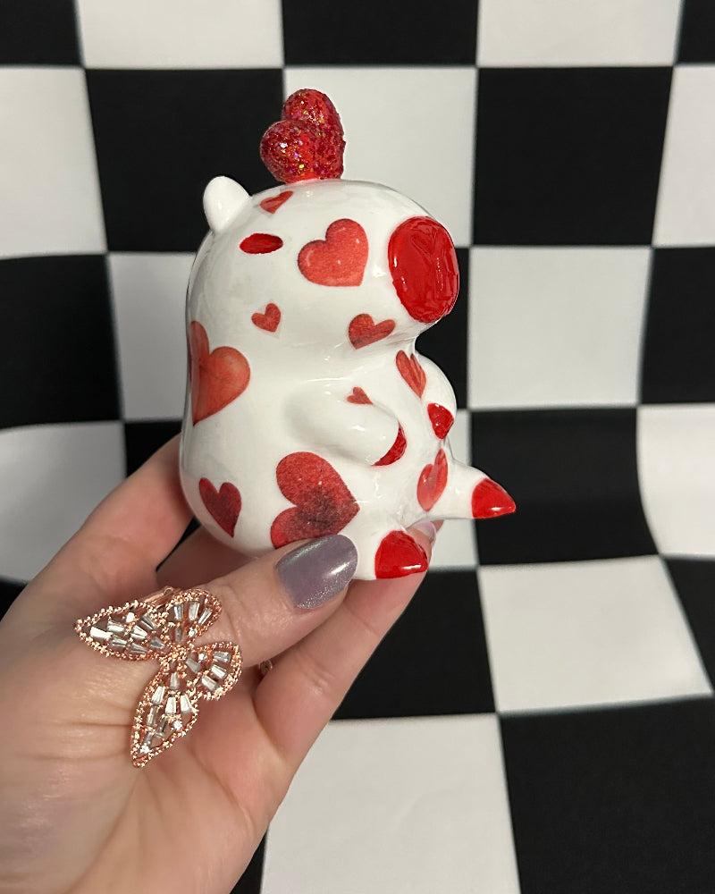 Hand holding a small white figurine with red heart patterns against a black and white checkered background.