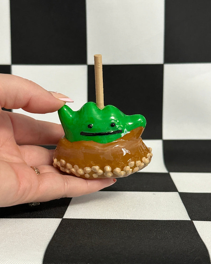 Hand holding a small green creature on a donut with a checkered background