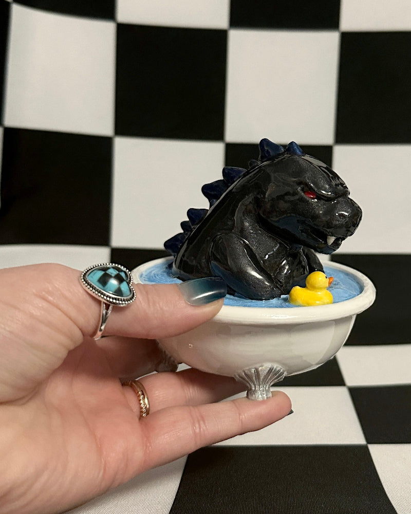 Hand holding a small bowl with a black dragon figurine against a checkered background