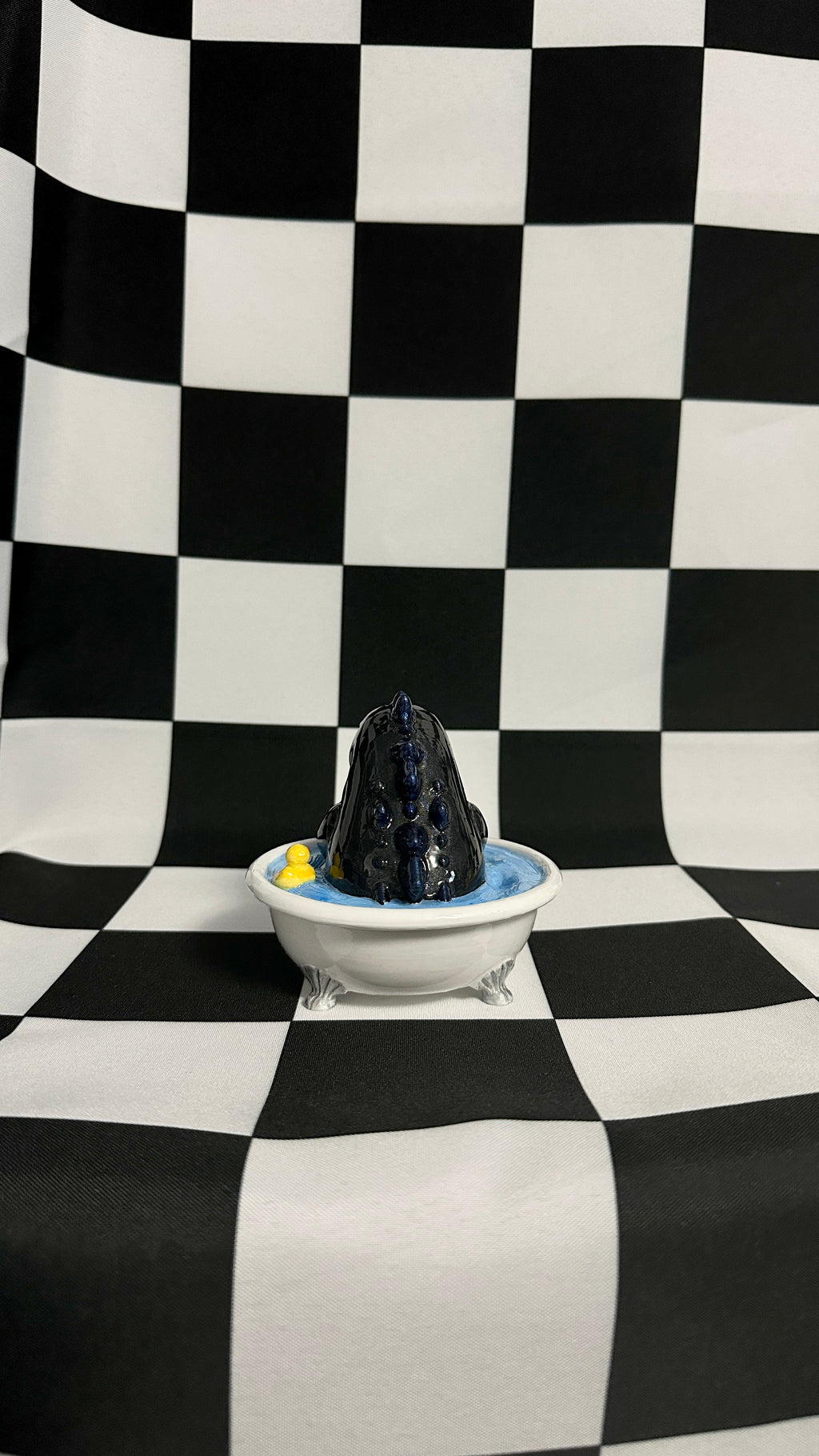 Black volcanic sculpture in a white bowl on a checkered black and white background