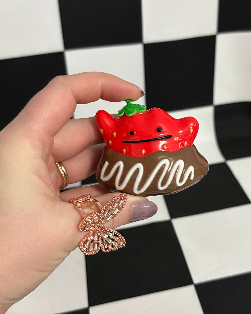 Hand holding a small red and brown object against a black and white checkered background