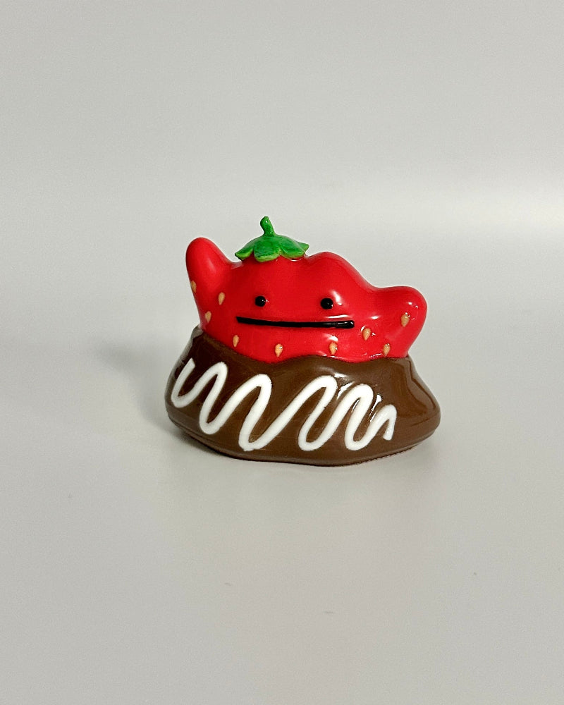 Small chocolate dessert figurine with a strawberry on top against a white background