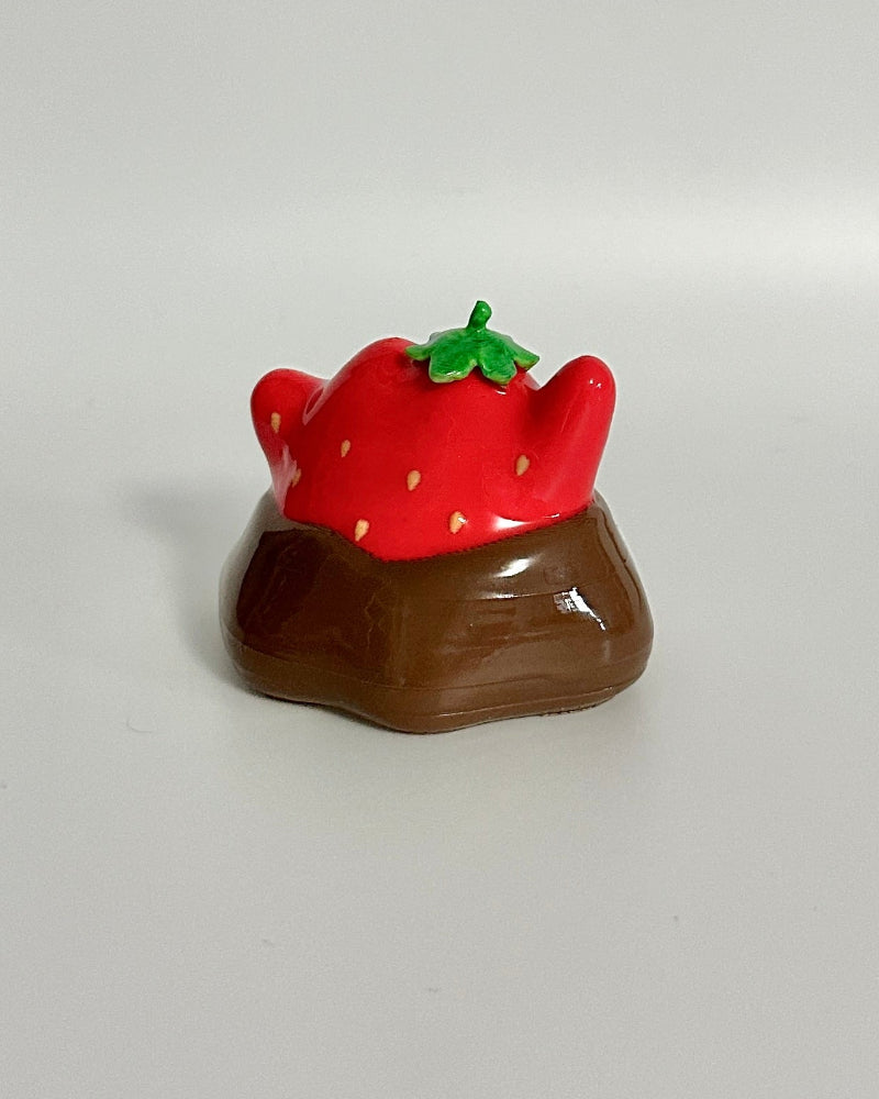 Small chocolate figurine with a red strawberry on top against a white background