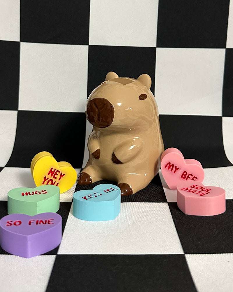 capybara figurine surrounded by colorful heart-shaped tokens on a black and white checkered background