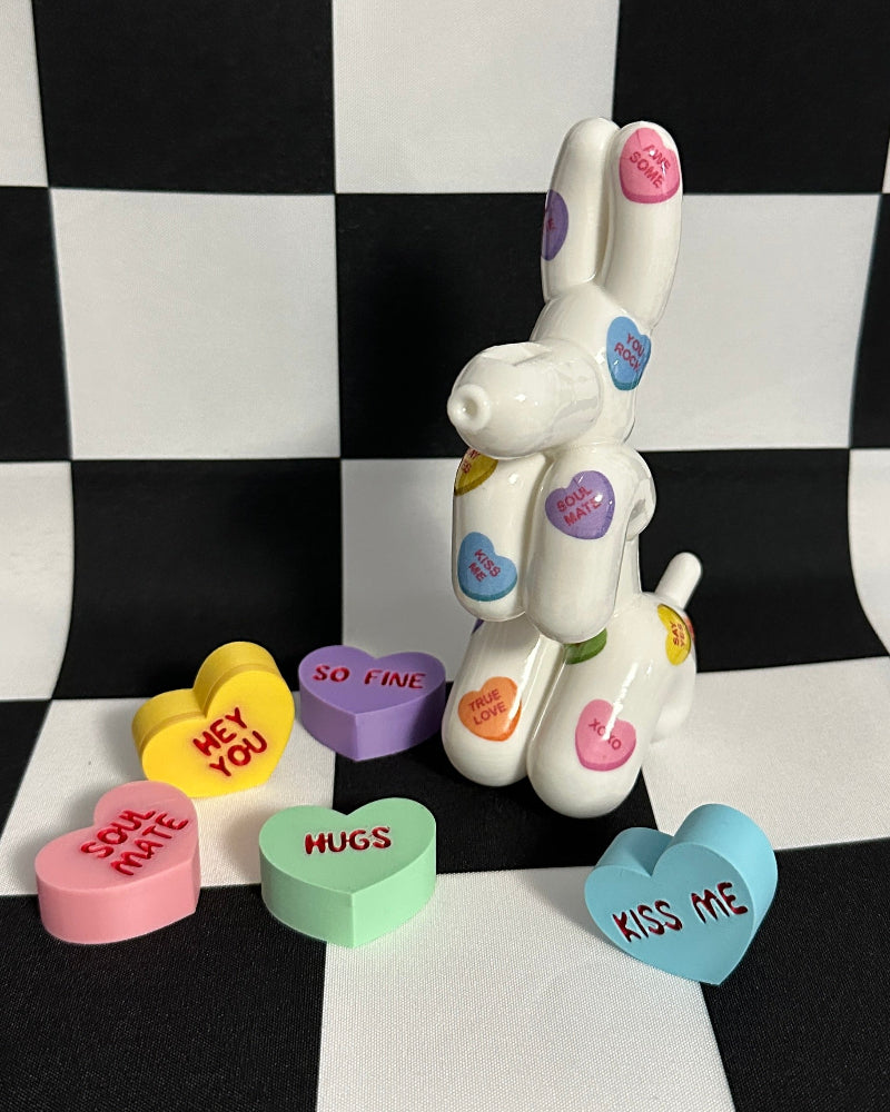 Decorative dog figurine with colorful heart-shaped candies on a black and white checkered background