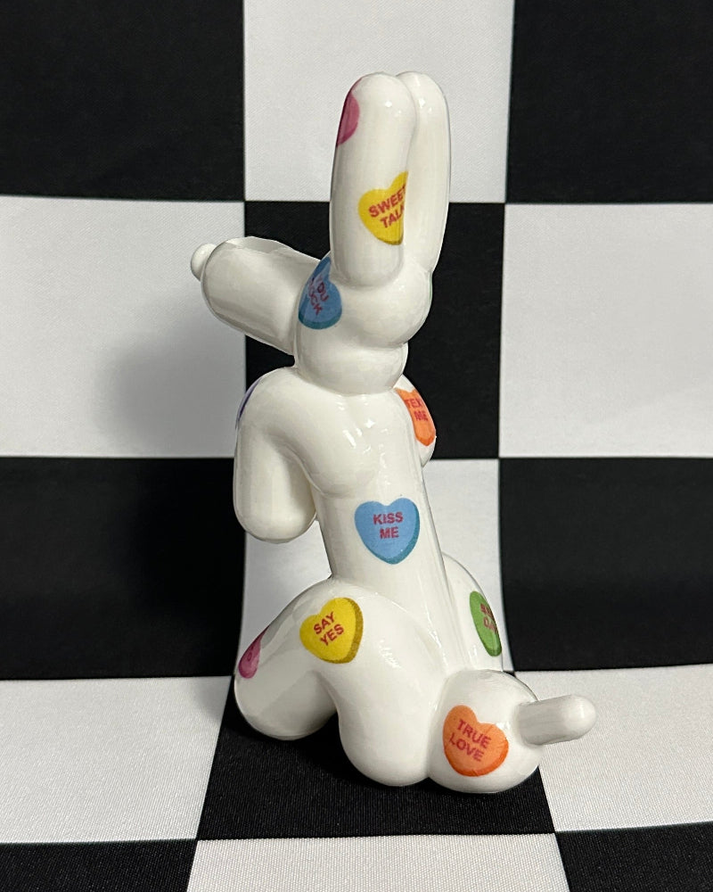 White ceramic dog figurine with colorful heart-shaped buttons on a black and white checkered background