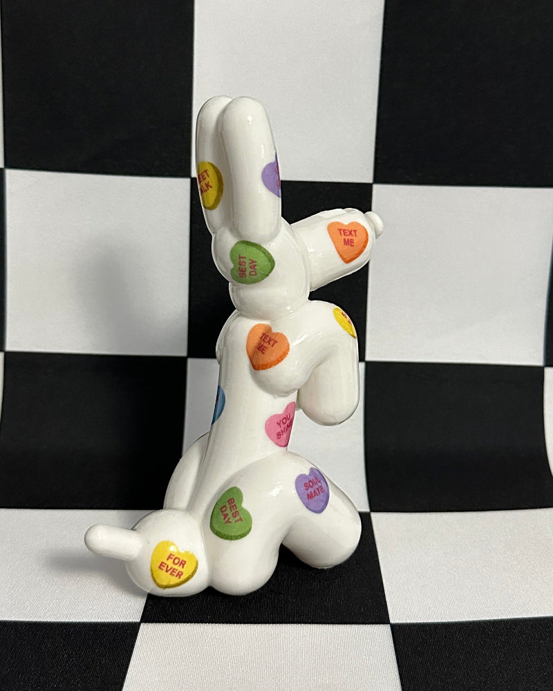 White ceramic dog figurine with colorful heart patterns on a black and white checkered background